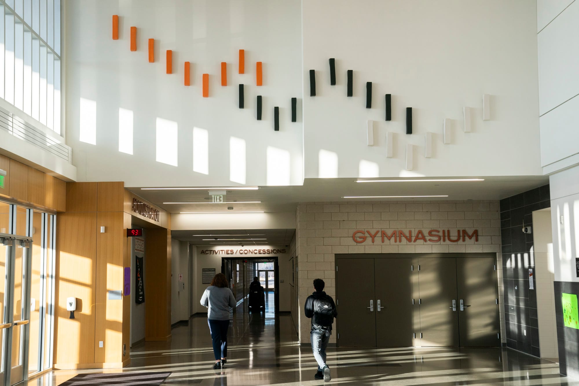 A ceramic pottery art installation is seen on a wall in a high school lobby. Its colors are orange, black and white, the school's colors. 
