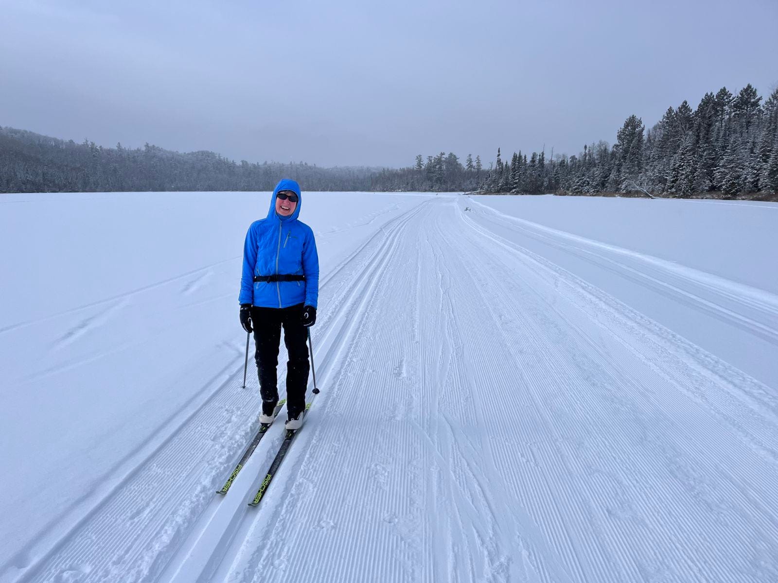 Woman smiles while cross-country skiing on a snowy lake. 