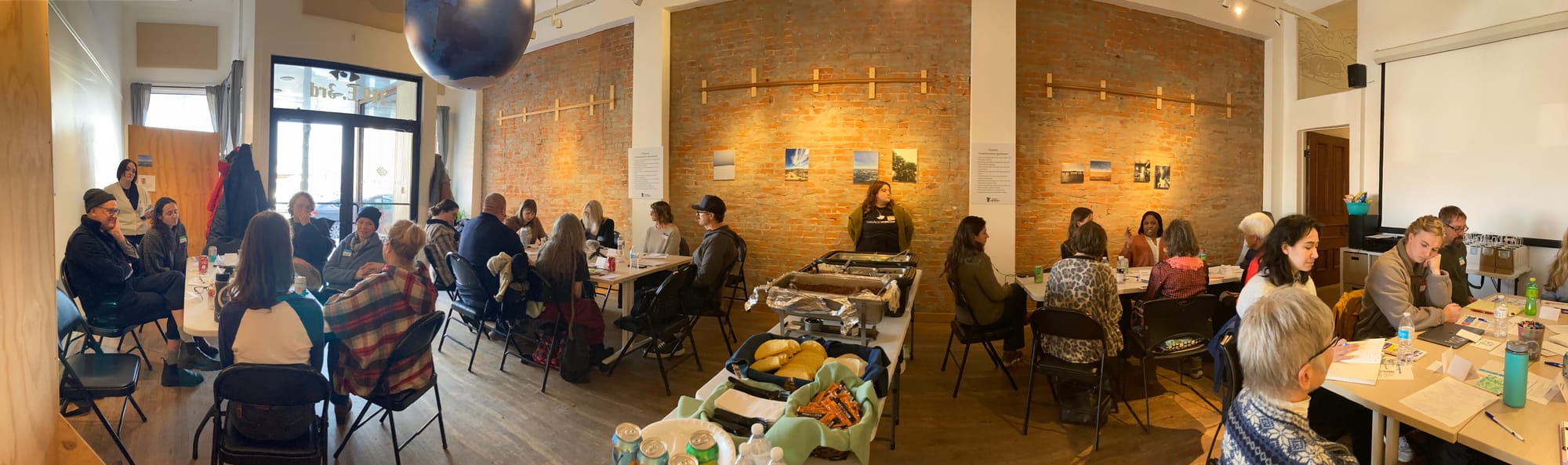 Panoramic view of a meeting space with people seated at tables engaged in conversations. 