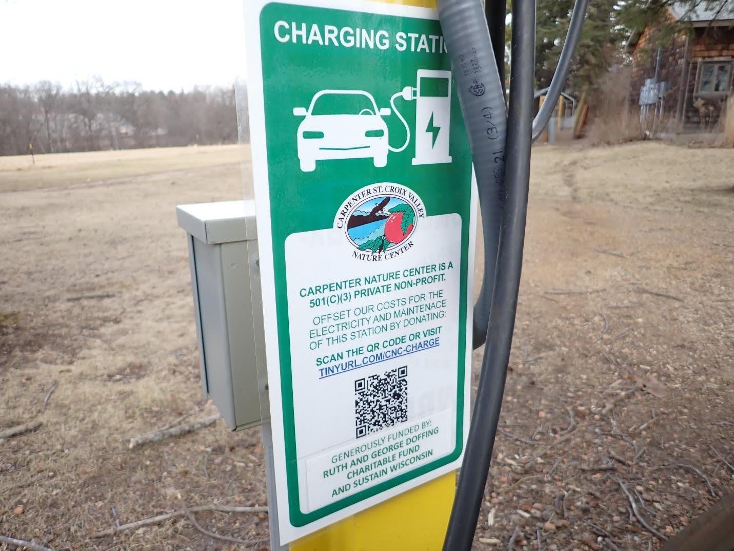 A sign tells people how to donate. The sign is green with a picture of a car connected to a charger. It includes a QR code that people can scan to get to the donation website.