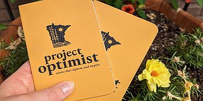 Hand holds two yellow Project Optimist notebooks