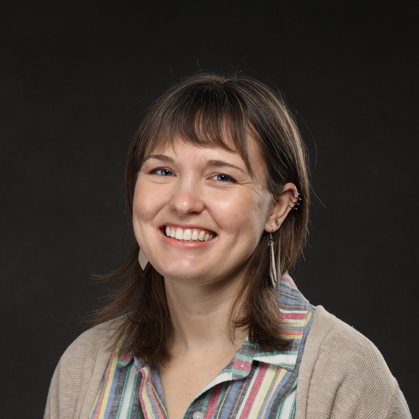 Photo of Project Optimist founder Nora Hertel smiling with a mulitcolor stripped shirt and shoulder length brown hair and bangs. 