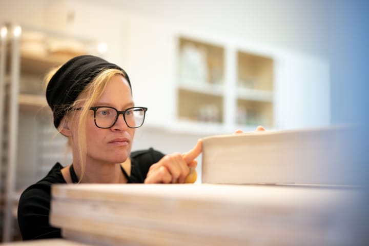 Woman uses her hands to sculpt a piece of pottery in her studio.