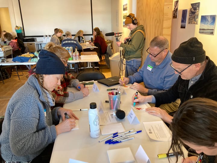 People sit around a table drawing art based on a prompt