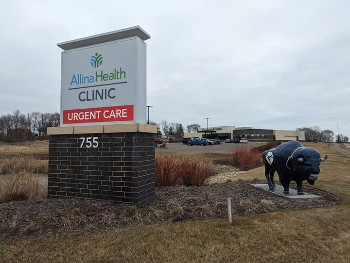 A buffalo statue and a sign for a health clinic are pictured in the foreground while the clinic is in the background.