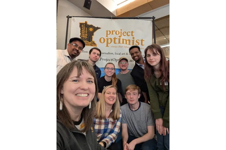 Nine people pose for a photo in front of banners for the two news organizations that co-hosted the event. 