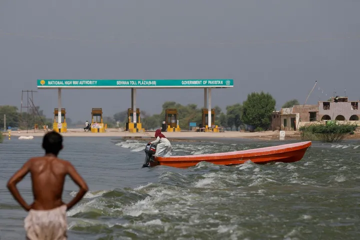 A man rides a boat past a toll plaza amid flood water on main Indus highway, following rains and floods during the monsoon se