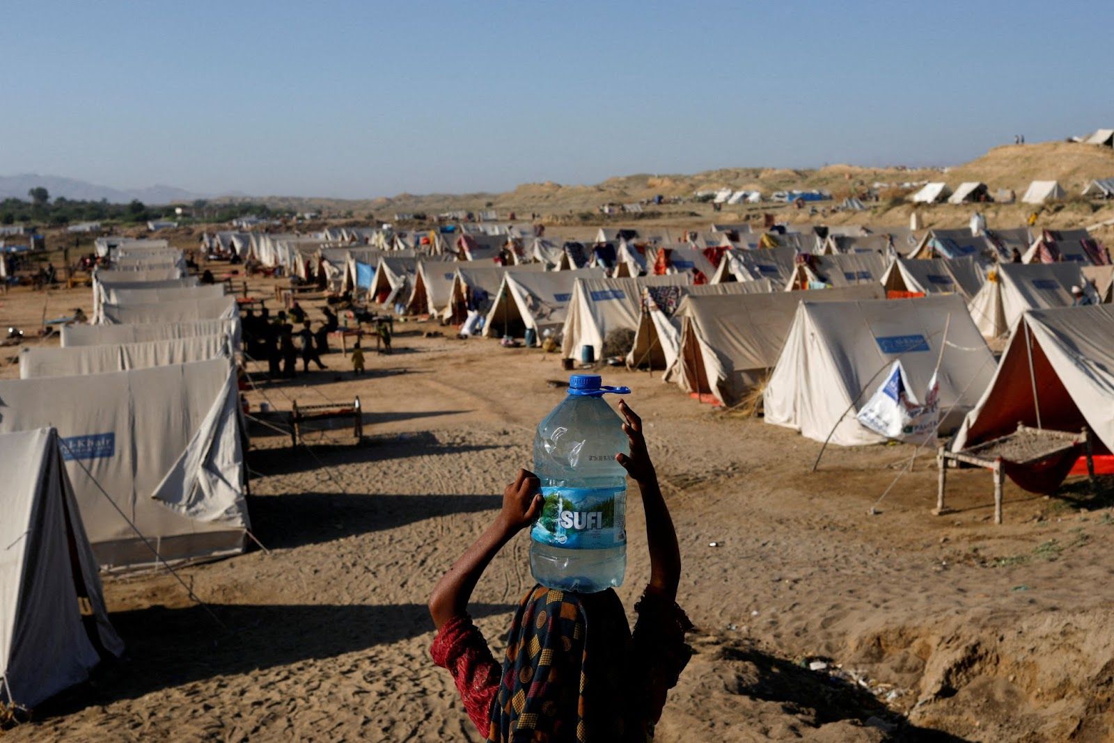 A displaced girl carries a bottle of water she filled from nearby stranded flood-waters, as her family takes refuge in a camp, in Sehwan, Pakistan, September 30, 2022. (REUTERS/Akhtar Soomro/File Photo)